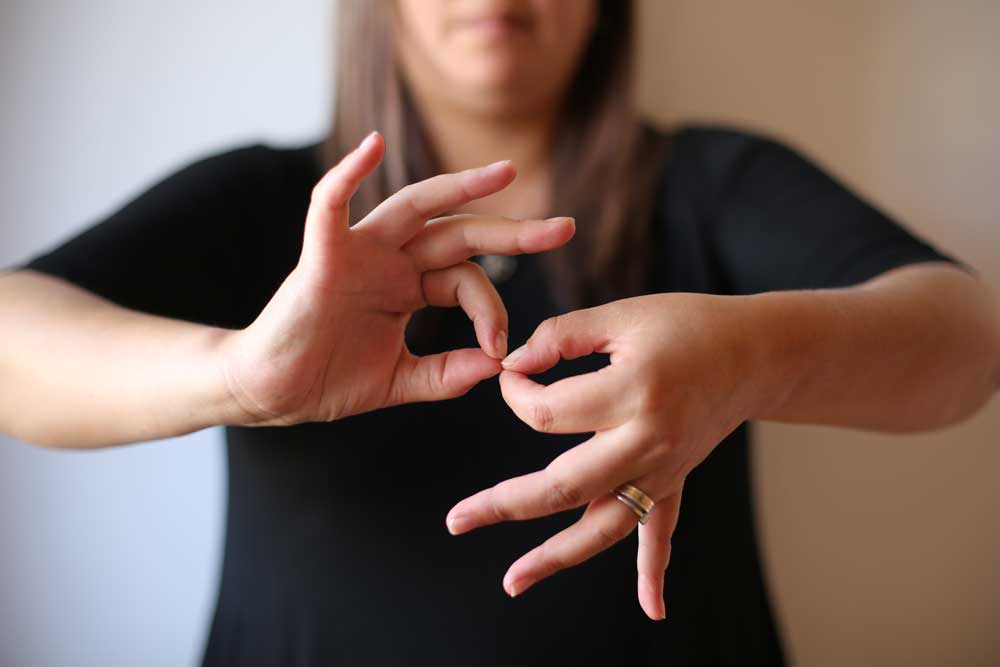 Foto de una intérprete de lengua de señas, y se ve en primer plano sus manos que hacen la seña de interpretación.
