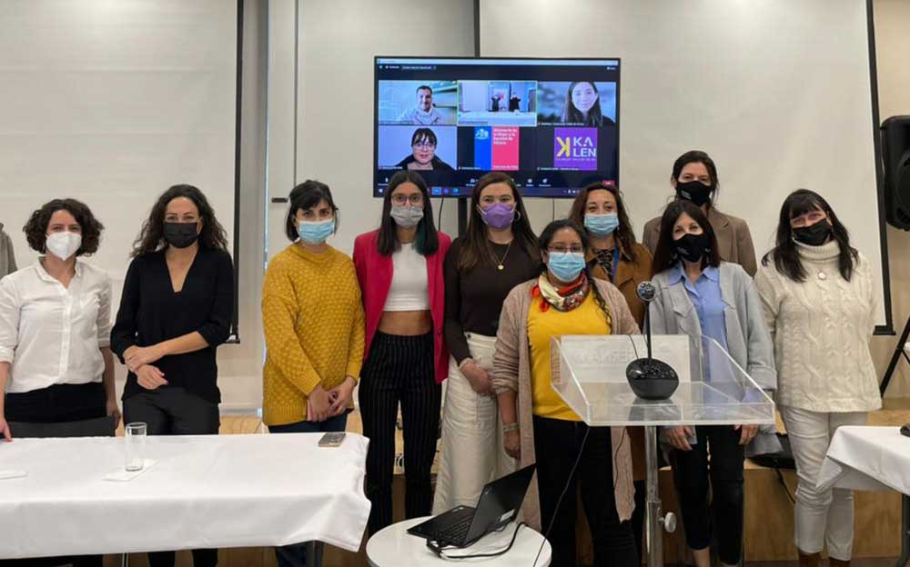 Foto de un grupo de aproximadamente 10 mujeres sonriendo y mirando a la cámara. Están en una sala de reuniones del ministerio de la mujer.