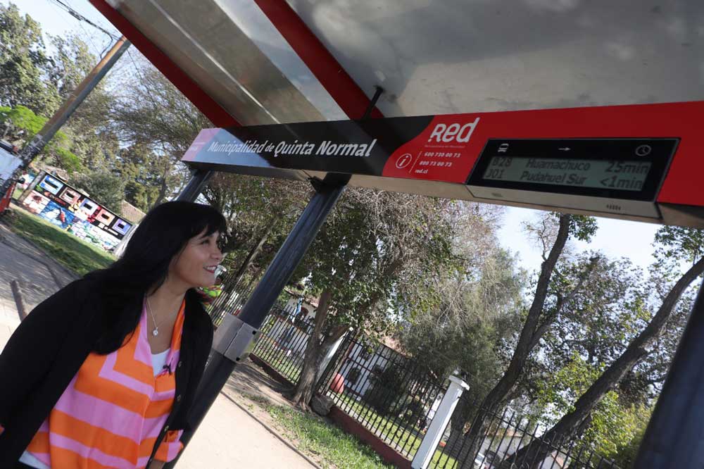 Foto de una mujer observando una pantalla digital que tiene el paradero y donde dice el tiempo de espera del próximo bus.