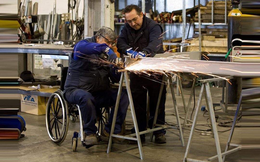 Foto de una persona en silla de ruedas soldado una mesa dentro de un taller.