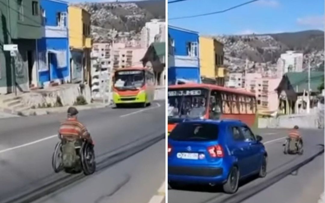 Pantallazo de un video donde aparece una persona en silla de ruedas bajando por una calle en un cerro de valparaíso, y de frente hay una micro y atrás de él viene un auto que lo intenta adelantar.