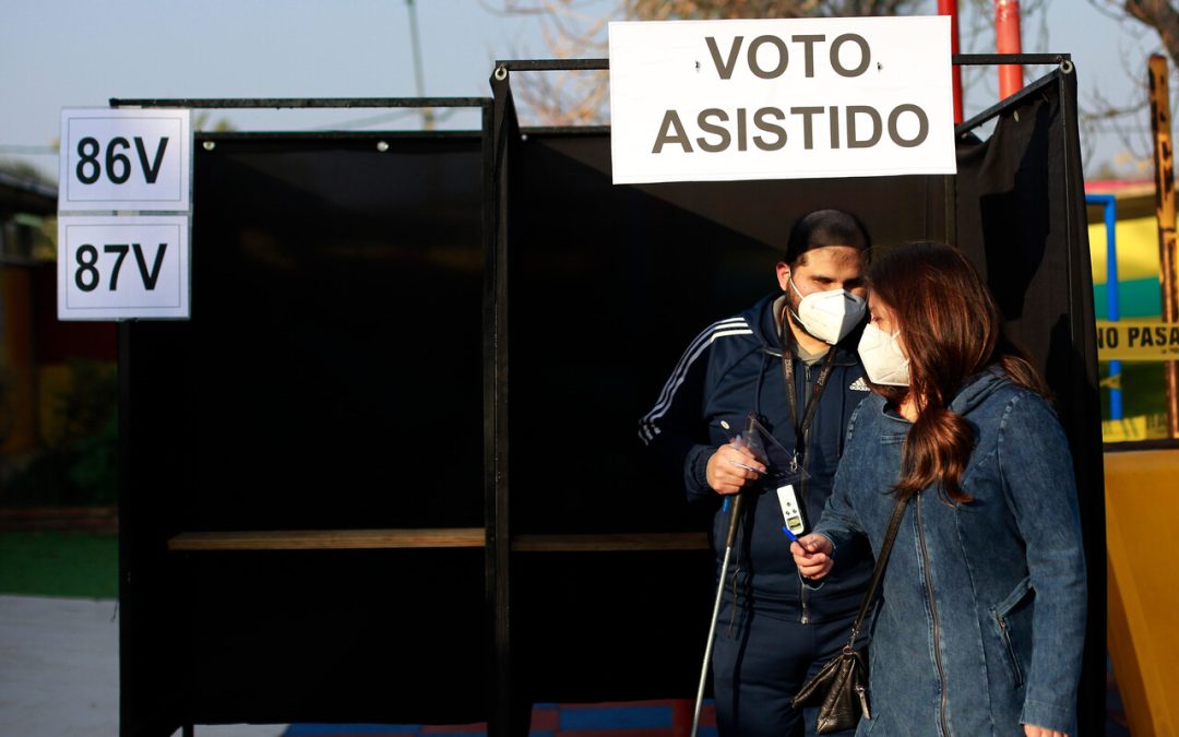 Foto de una persona ciega siendo acompañada por otra persona en la urna de votación.